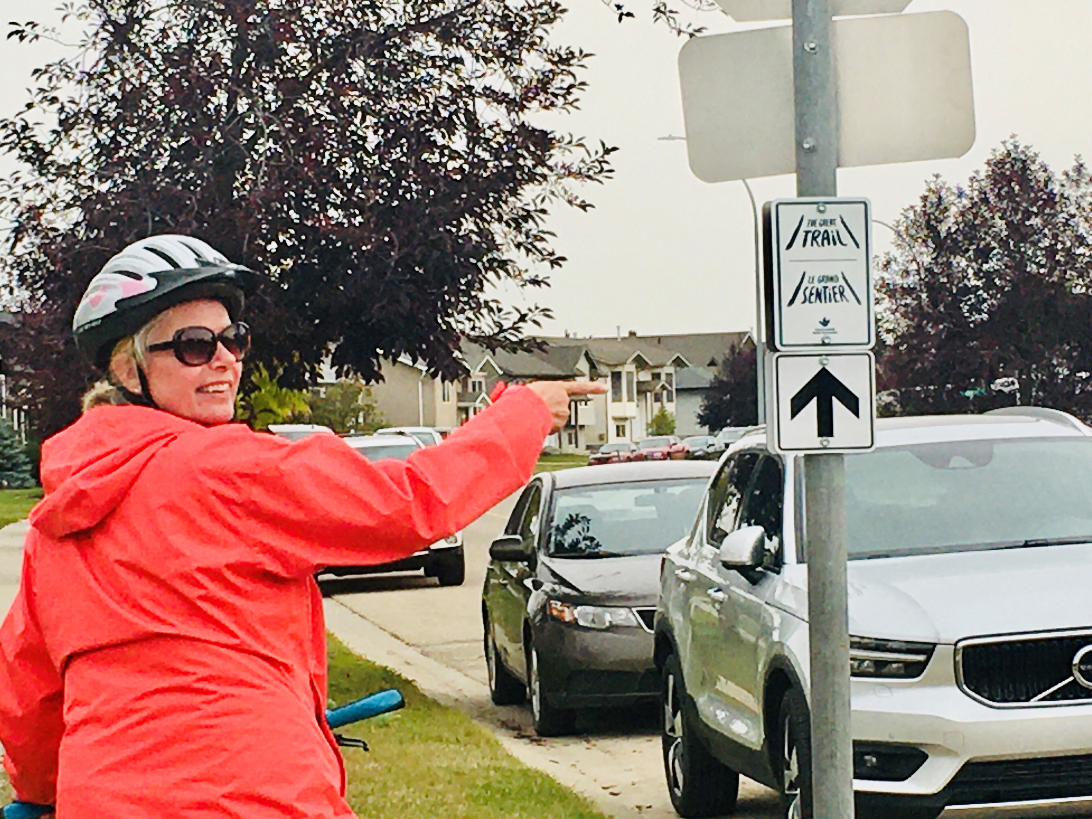 Person wearing a red coat and bike helmet pointing at a directional sign for The Great Trail