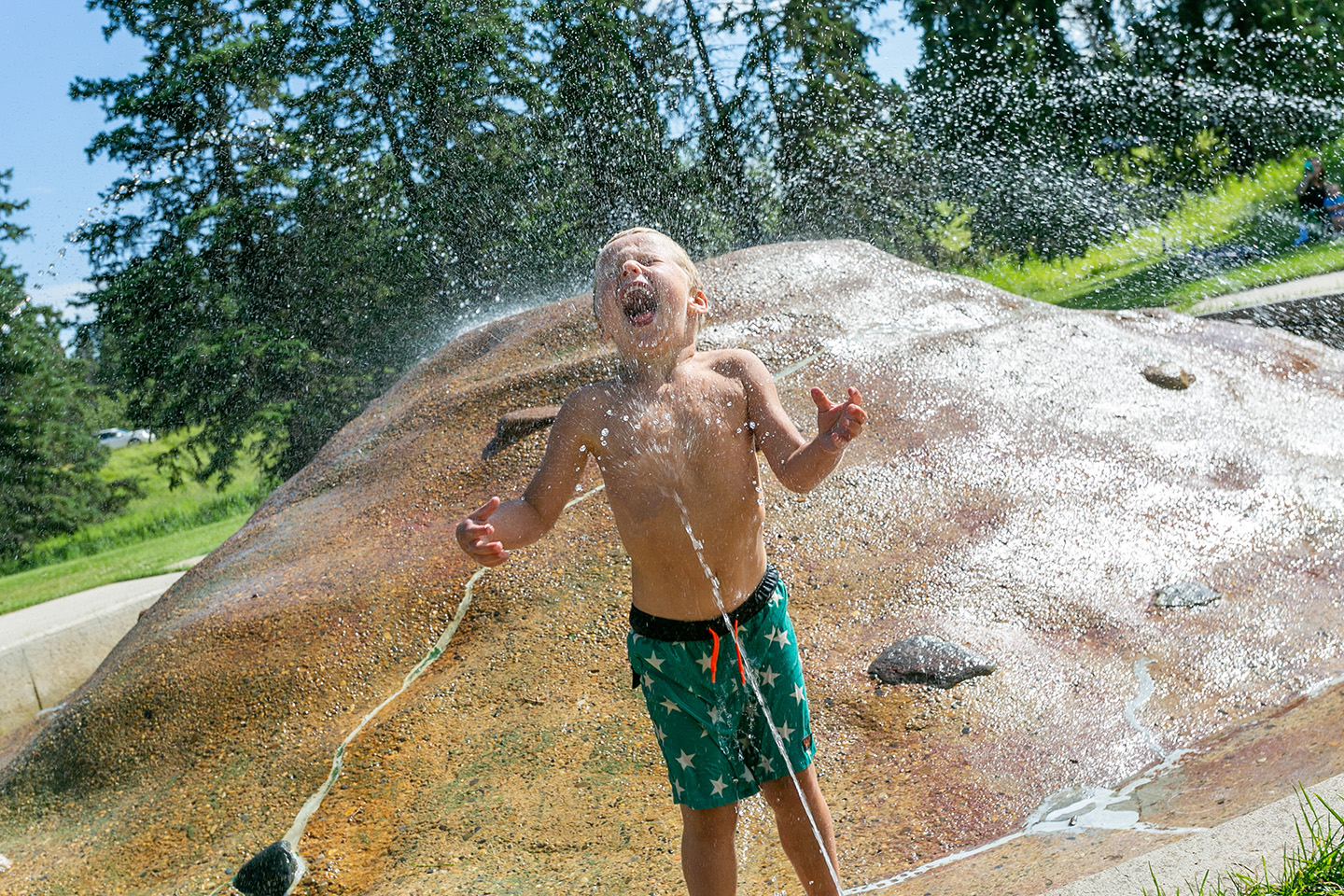 Youth playing in the water fountain at Kin Kanyon, he's being sprayed in the face with a big grin