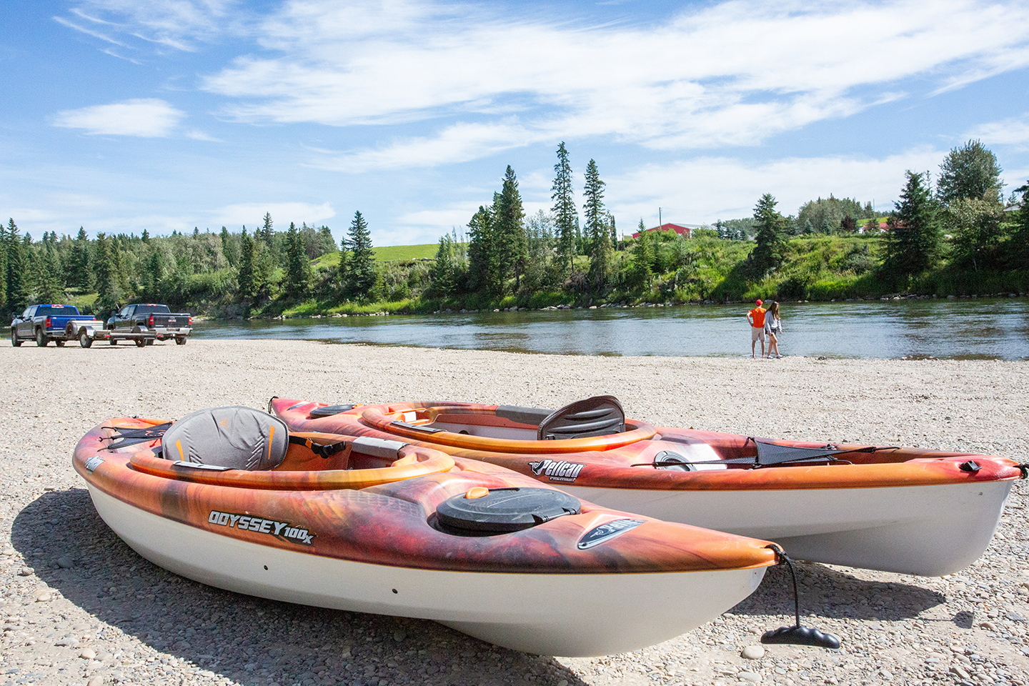 Two orange kyaks rest on shore of the Red Deer River on a bright sunny day.